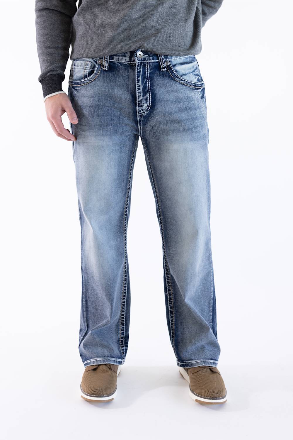 Front view of a male model wearing True Luck Mac Loose Straight medium-wash jeans with light fading and whiskering, a grey long-sleeve sweater, and brown casual shoes against a plain white background.