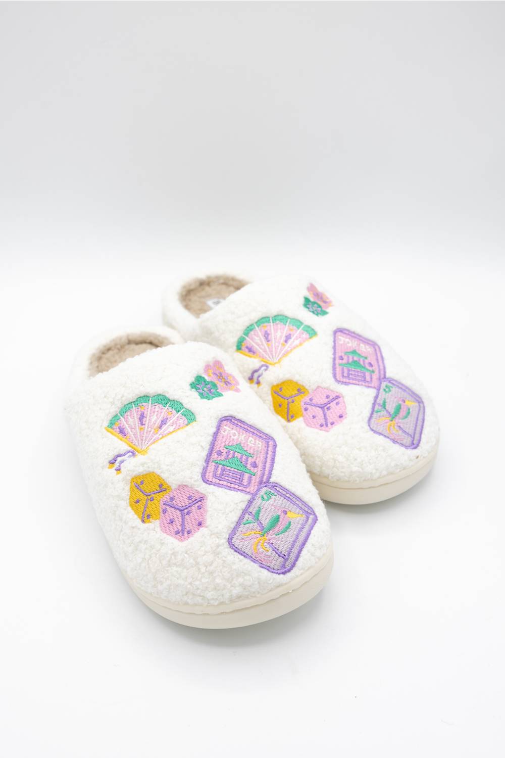 A pair of white sherpa slip-on slippers decorated with colorful embroidered majong and fan motifs on the sides, shown on a clean white background.