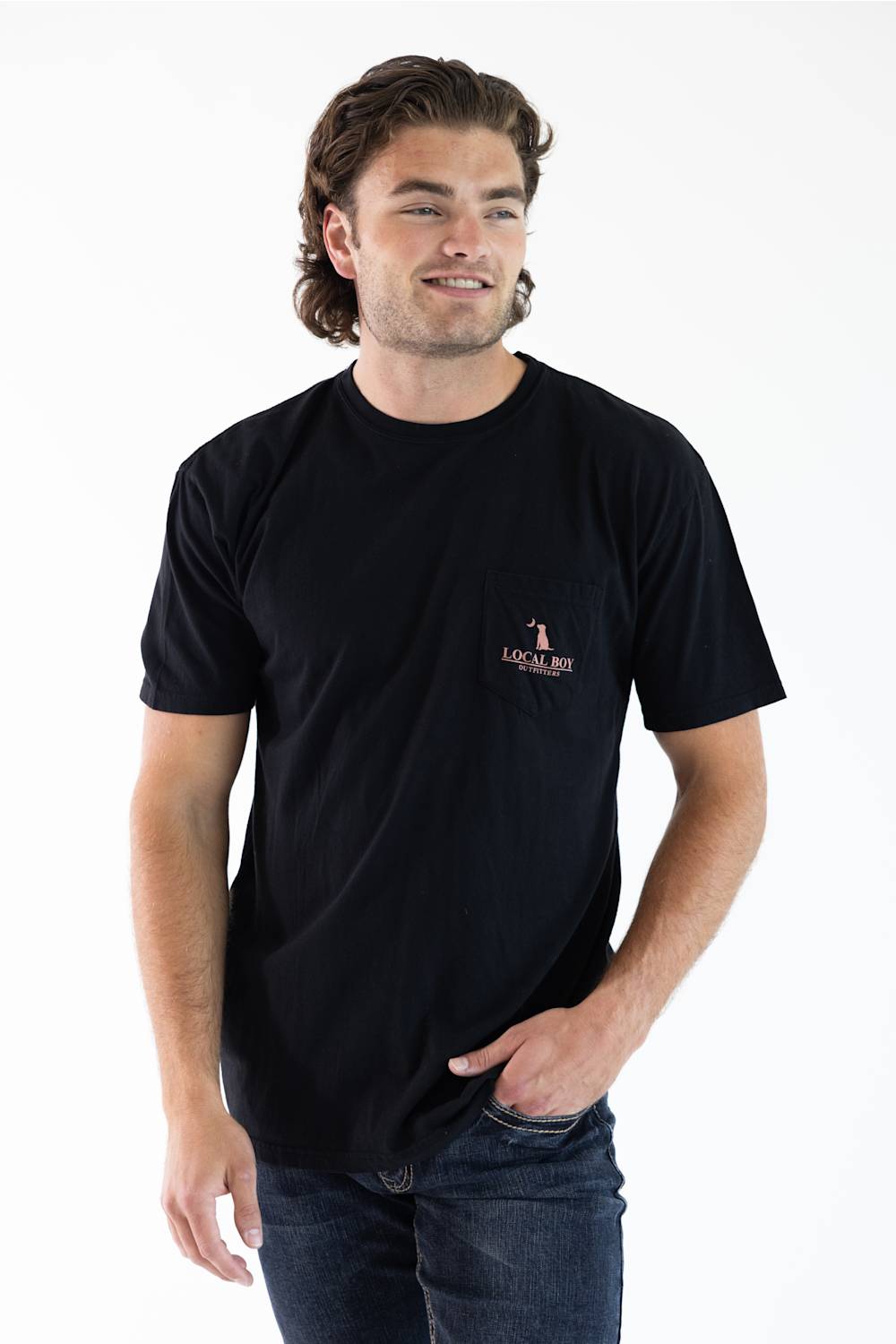 A man wearing a black short-sleeve crewneck t-shirt with a small 'lOCAL BOY' logo printed on the left chest, paired with dark blue jeans, against a plain white background.