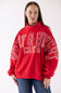 A woman wearing a bright red sweatshirt with mERRY & bRIGHT text in pink and gold on the front, paired with blue jeans, against a plain white background.
