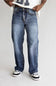 A person wearing a pair of relaxed-fit medium-wash blue denim jeans with whiskering and faded details, styled with a white t-shirt and black and white sneakers against a light gray studio background.