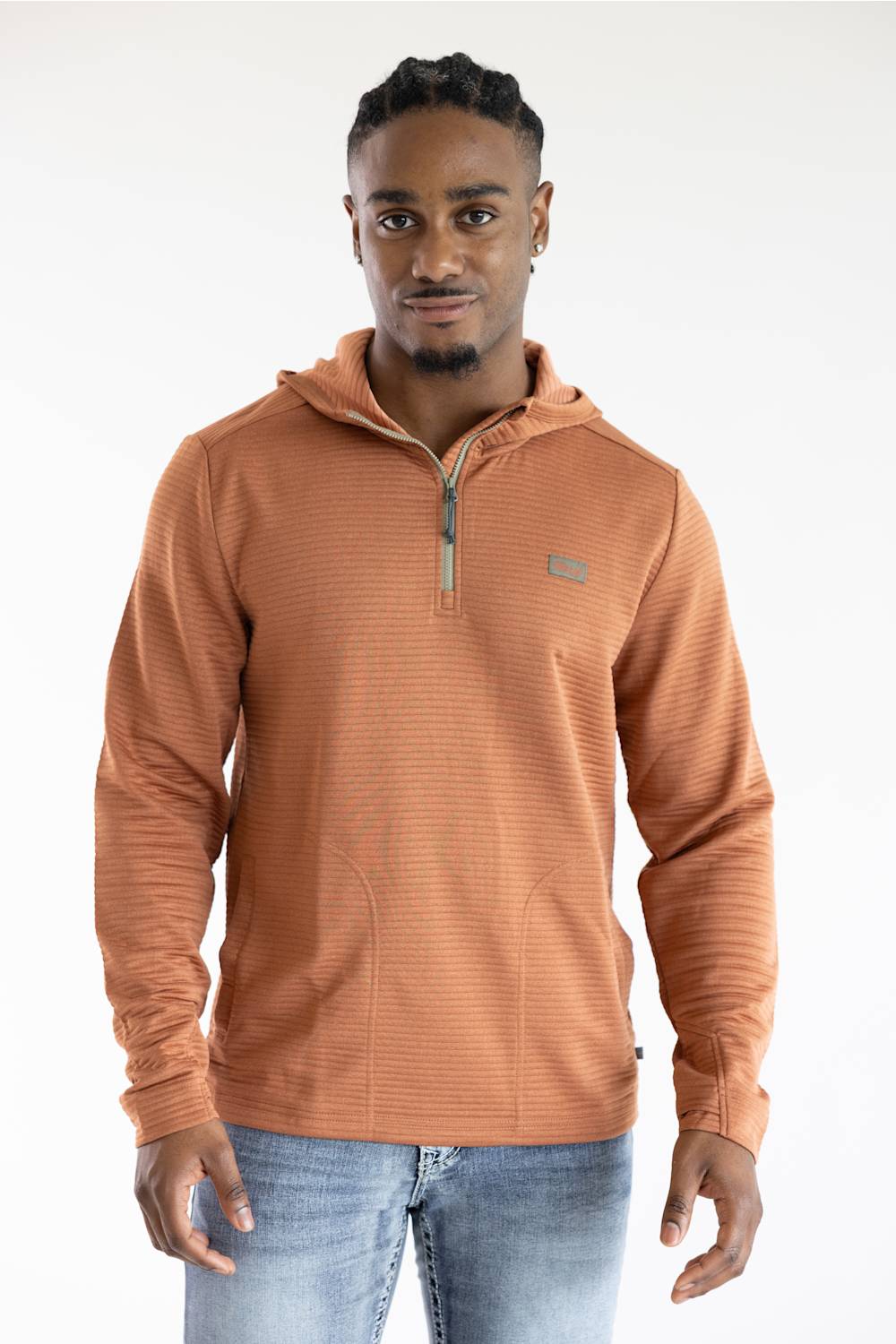 A man wearing a ribbed, quarter-zip pullover hoodie in a warm terracotta orange color, paired with blue jeans, photographed against a clean white studio background.