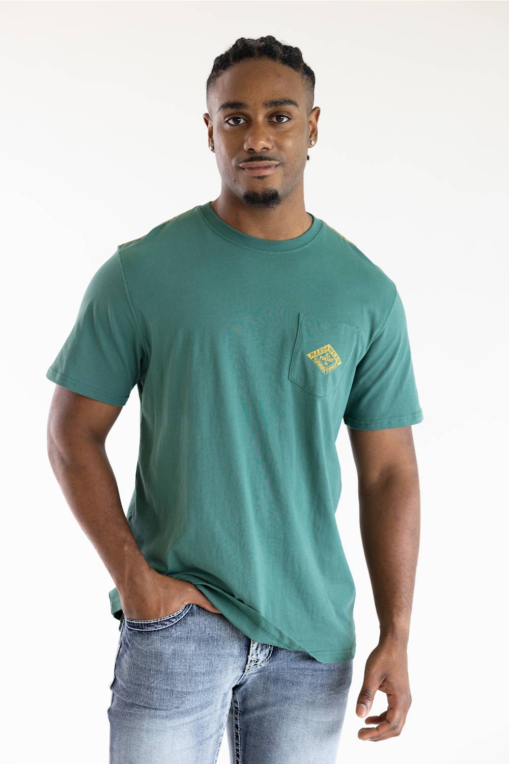 A man wearing a teal green pocket t-shirt with a small yellow graphic on the chest, paired with light blue jeans, standing against a plain white background.
