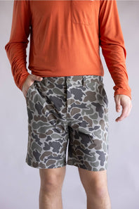 Marsh Wear Prime Hagood 8” Shorts for Men in Green Mallard Camo; Person wearing an orange long-sleeve shirt and camouflage shorts on a plain background