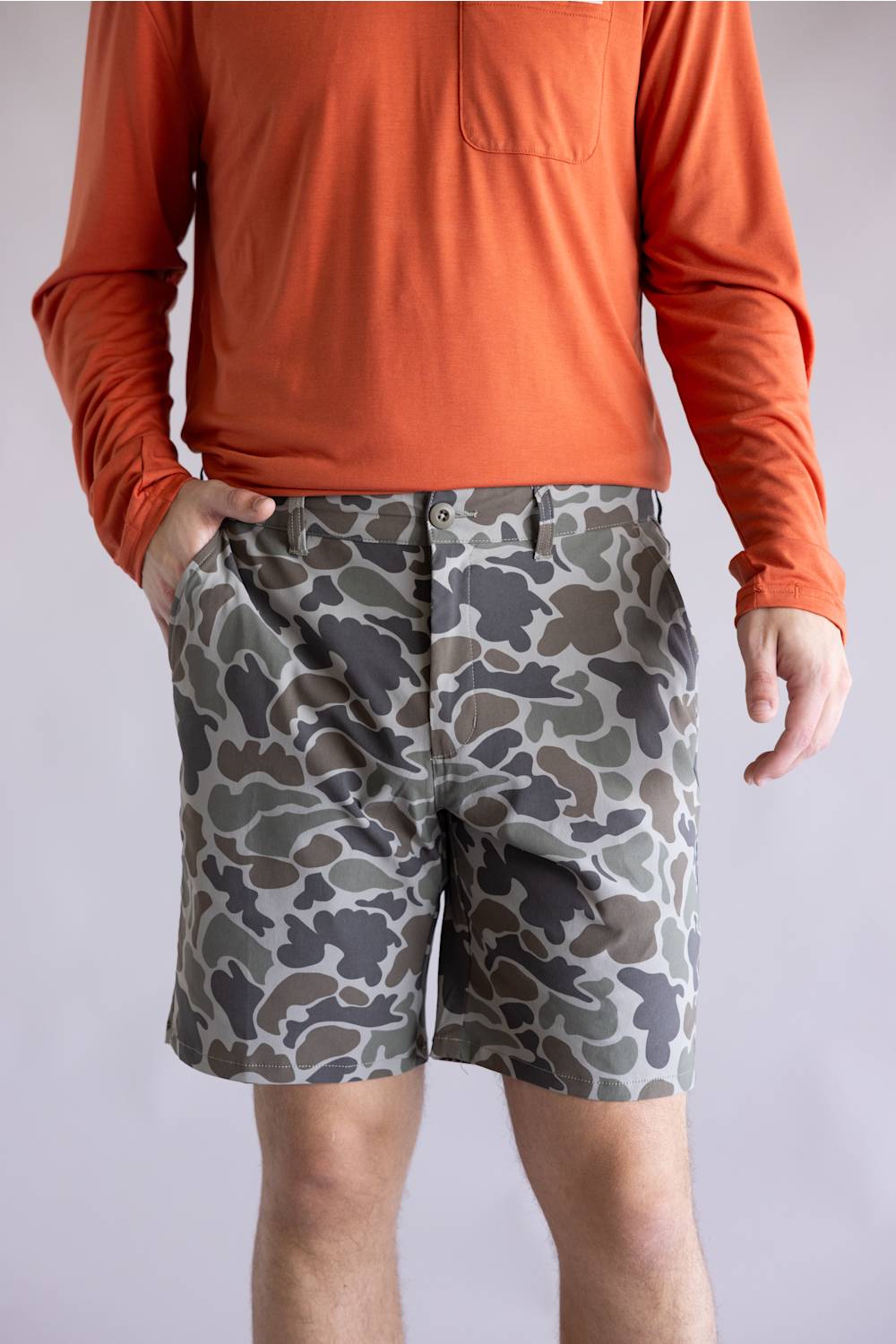 Marsh Wear Prime Hagood 8” Shorts for Men in Green Mallard Camo; Person wearing an orange long-sleeve shirt and camouflage shorts on a plain background