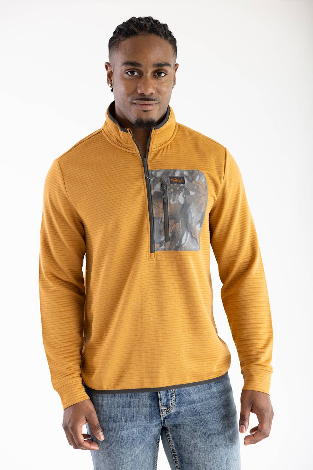 Front-facing studio shot of a model wearing the Marsh Wear Sullivan Quarter Zip Pullover in Buckthorn Brown, featuring a textured ribbed design, dark grey inner stand-up collar, front quarter-zip closure, and a zip chest pocket with a camouflage pattern accent, paired with light-wash blue jeans.
