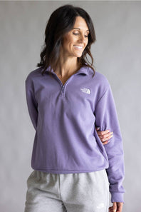 A woman wearing a lavender purple quarter-zip fleece pullover by The North Face, paired with light gray sweatpants, set against a neutral gray studio background.