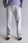 A person shown from the waist down wearing light gray heather sweatpants, a lavender sweatshirt, and black sneakers against a neutral gray studio background.