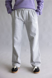A person shown from the waist down wearing light gray heather sweatpants, a lavender sweatshirt, and black sneakers against a neutral gray studio background.