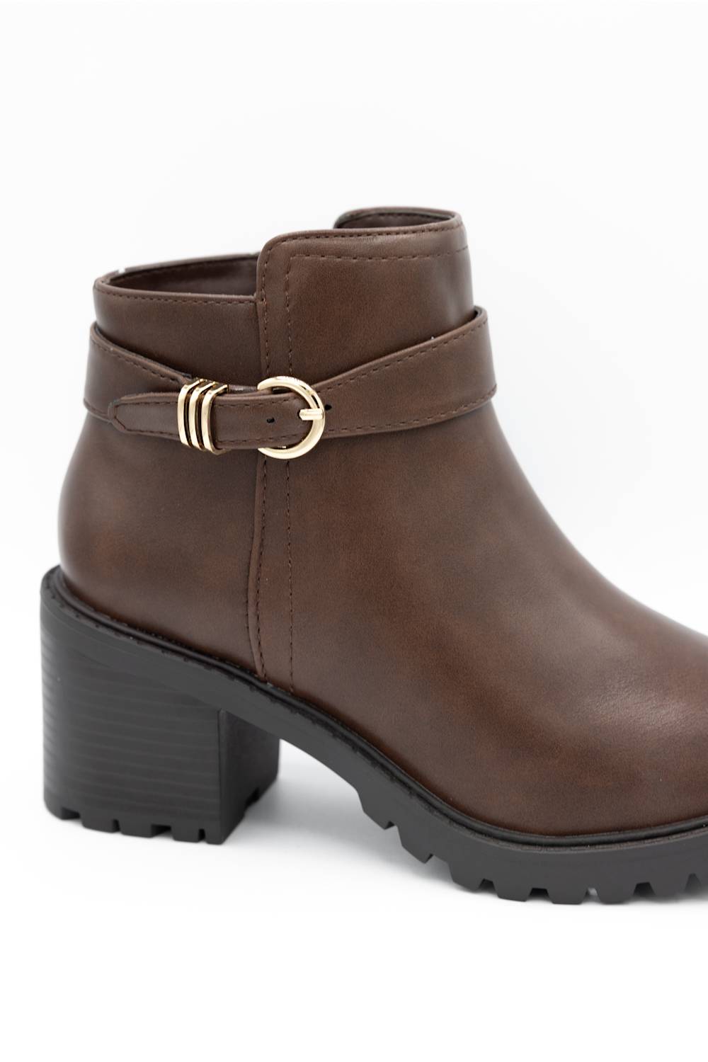 A brown faux-leather ankle boot with a chunky black block heel, a decorative strap across the ankle featuring a gold buckle, and a rugged lug sole, shown against a plain white background.