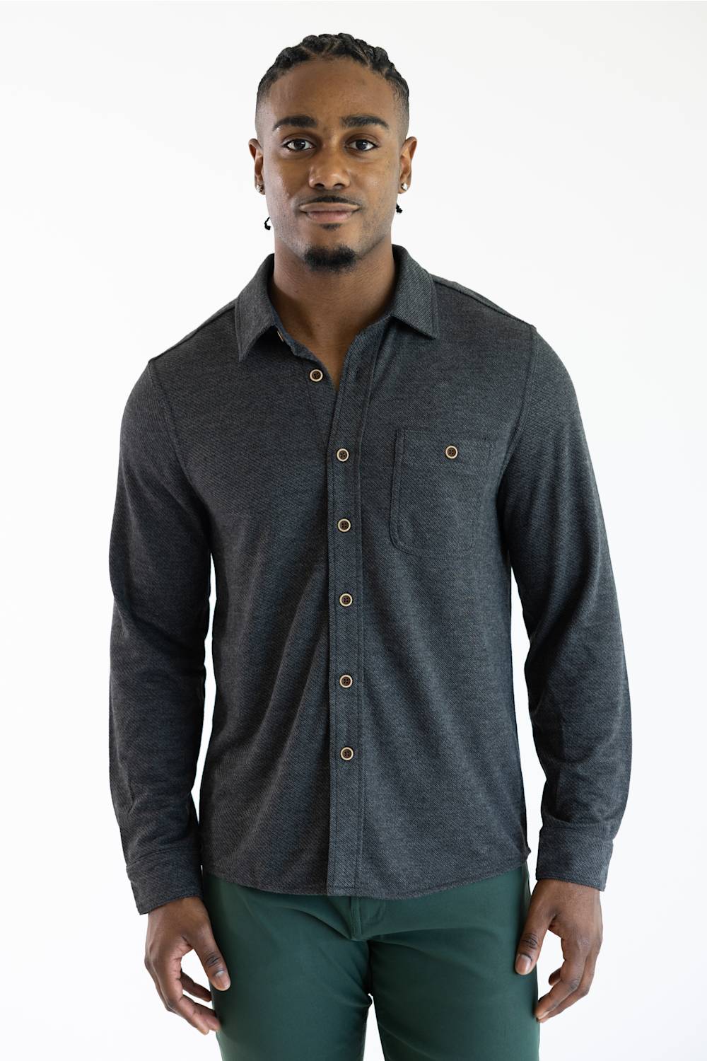 A man wearing a dark gray long-sleeve button-up shirt with brown buttons and a chest pocket, paired with green pants, against a plain white background.