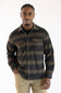 A man wearing a dark brown and black plaid button-down shirt with two chest pockets, paired with khaki pants, against a plain white background.