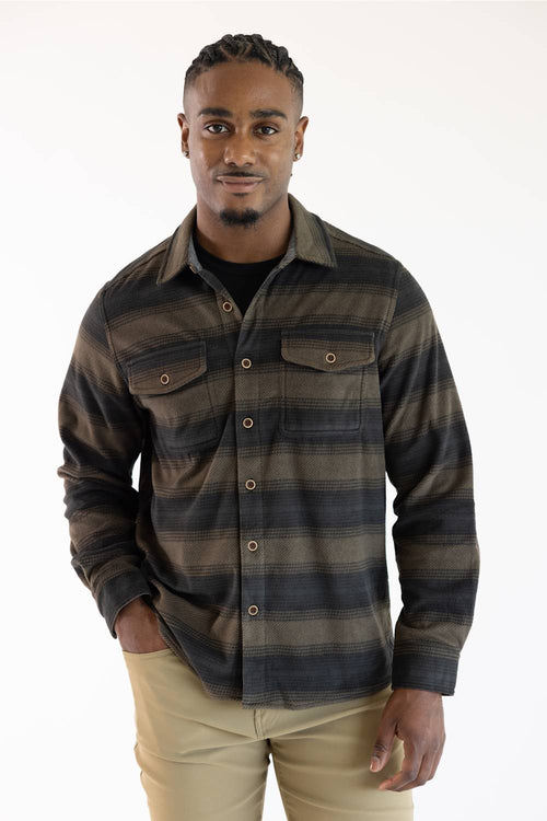A man wearing a dark brown and black plaid button-down shirt with two chest pockets, paired with khaki pants, against a plain white background.