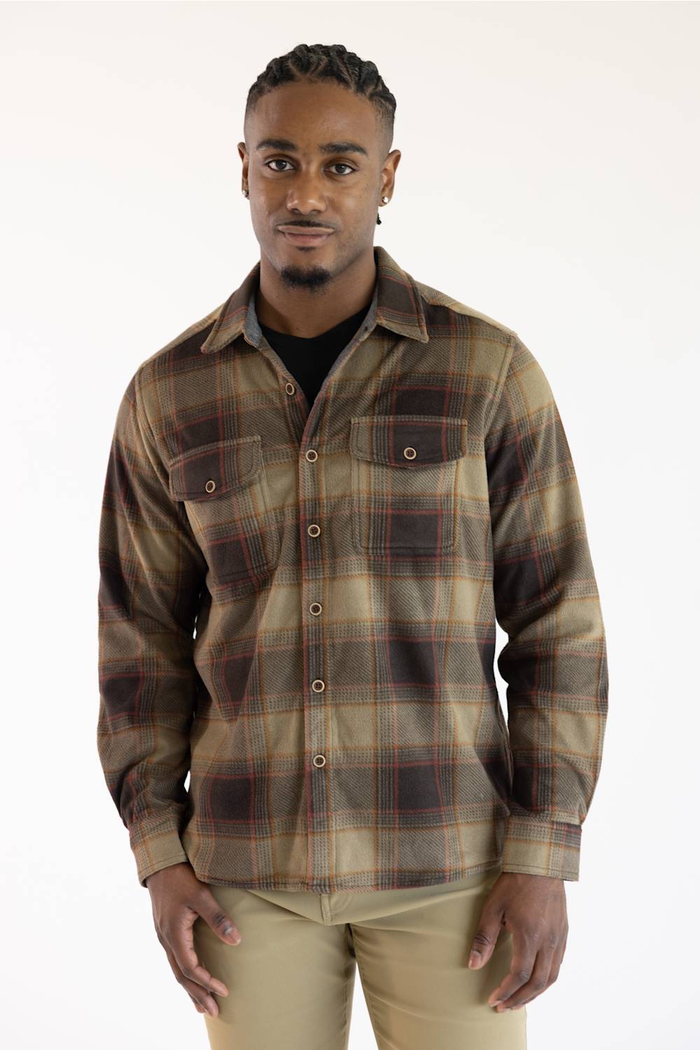 A man wearing a brown and beige plaid button-down shirt over a black undershirt, paired with khaki pants, standing against a plain white background.