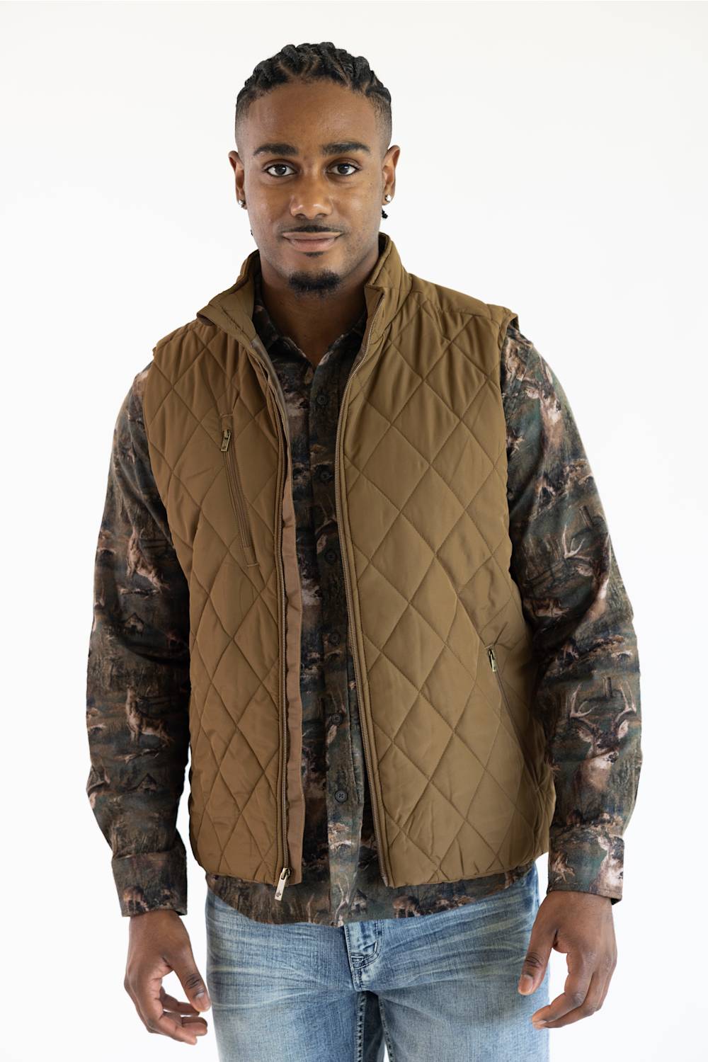 A man wearing a brown diamond-quilted zip-up vest over a camouflage long-sleeve shirt and blue jeans, standing against a plain white background.