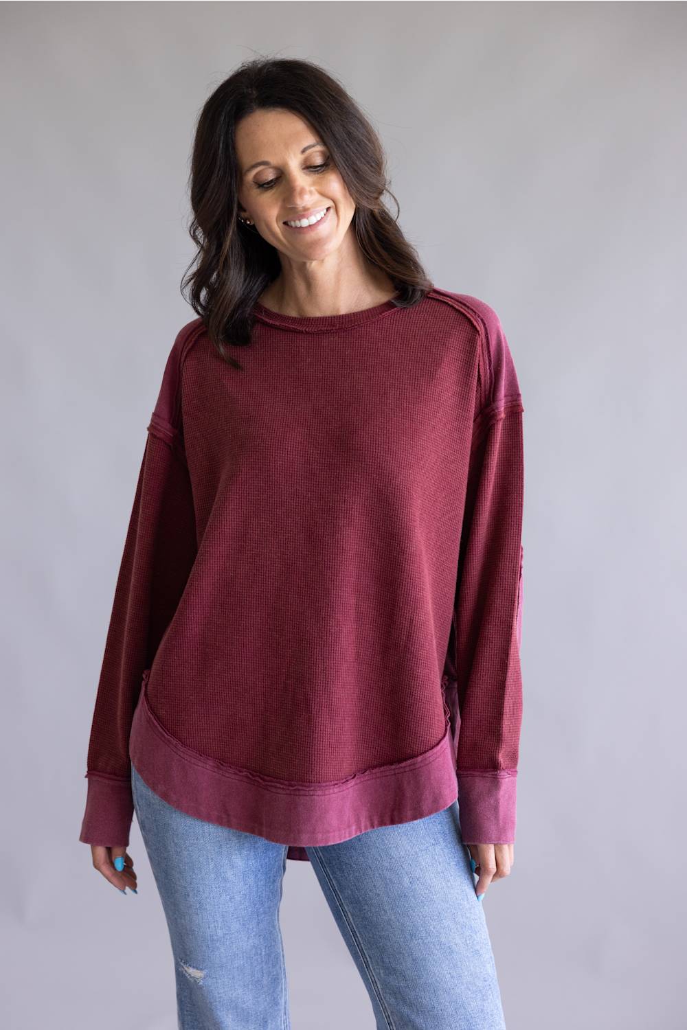 Woman wearing a maroon sweatshirt and blue jeans against a plain background