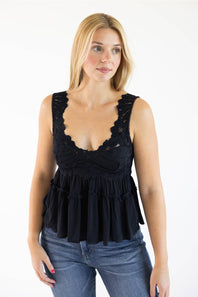 A woman modeling a black lace and ruffle sleeveless top paired with blue jeans, photographed against a plain white studio background.