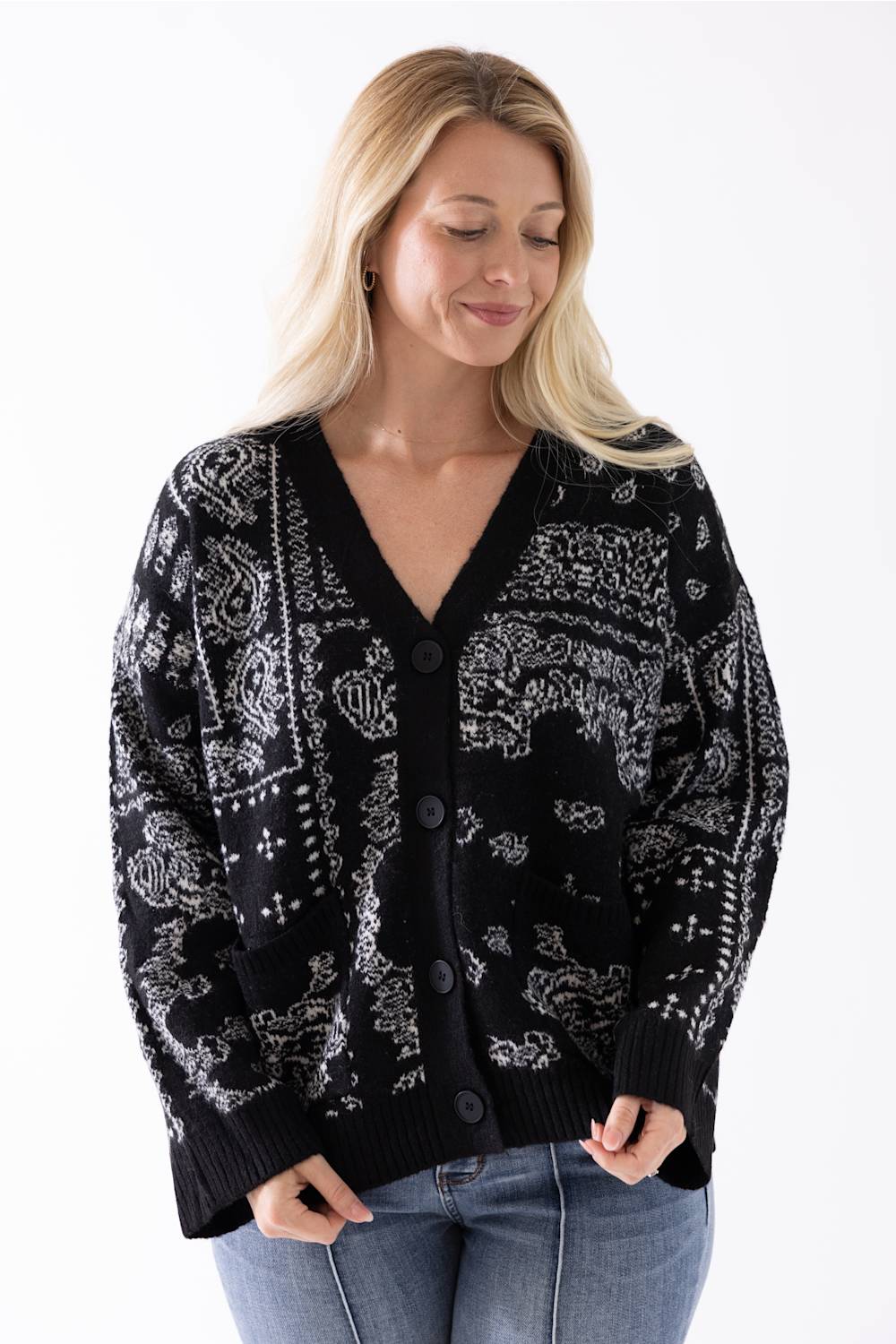 A woman wearing a black cardigan with a white paisley and tribal pattern, paired with blue jeans, against a plain white background.