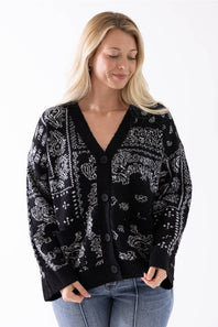 A woman wearing a black cardigan with a white paisley and tribal pattern, paired with blue jeans, against a plain white background.