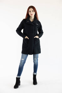A woman modeling a black mid-length coat with front pockets, paired with distressed blue jeans and black ankle boots, against a plain white studio background.