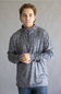 A man wearing a gray long-sleeve quarter-zip pullover with a subtle abstract pattern, paired with blue jeans, standing against a neutral gray background.