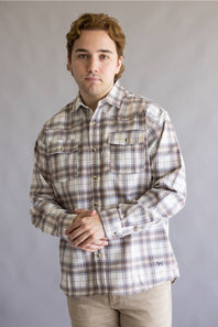 A man wearing a long-sleeve plaid button-down shirt in beige, brown, and white, paired with khaki pants, standing against a neutral gray studio background.