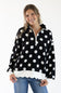 A woman modeling a black long-sleeve half-zip hoodie with large white polka dots and a white scalloped hem, paired with blue jeans against a plain white background.