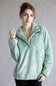 A woman wearing a light mint green textured fleece pullover with a half-zip collar, standing against a neutral gray studio background.