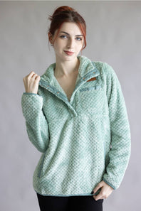 A woman wearing a light mint green textured fleece pullover with a half-zip collar, standing against a neutral gray studio background.