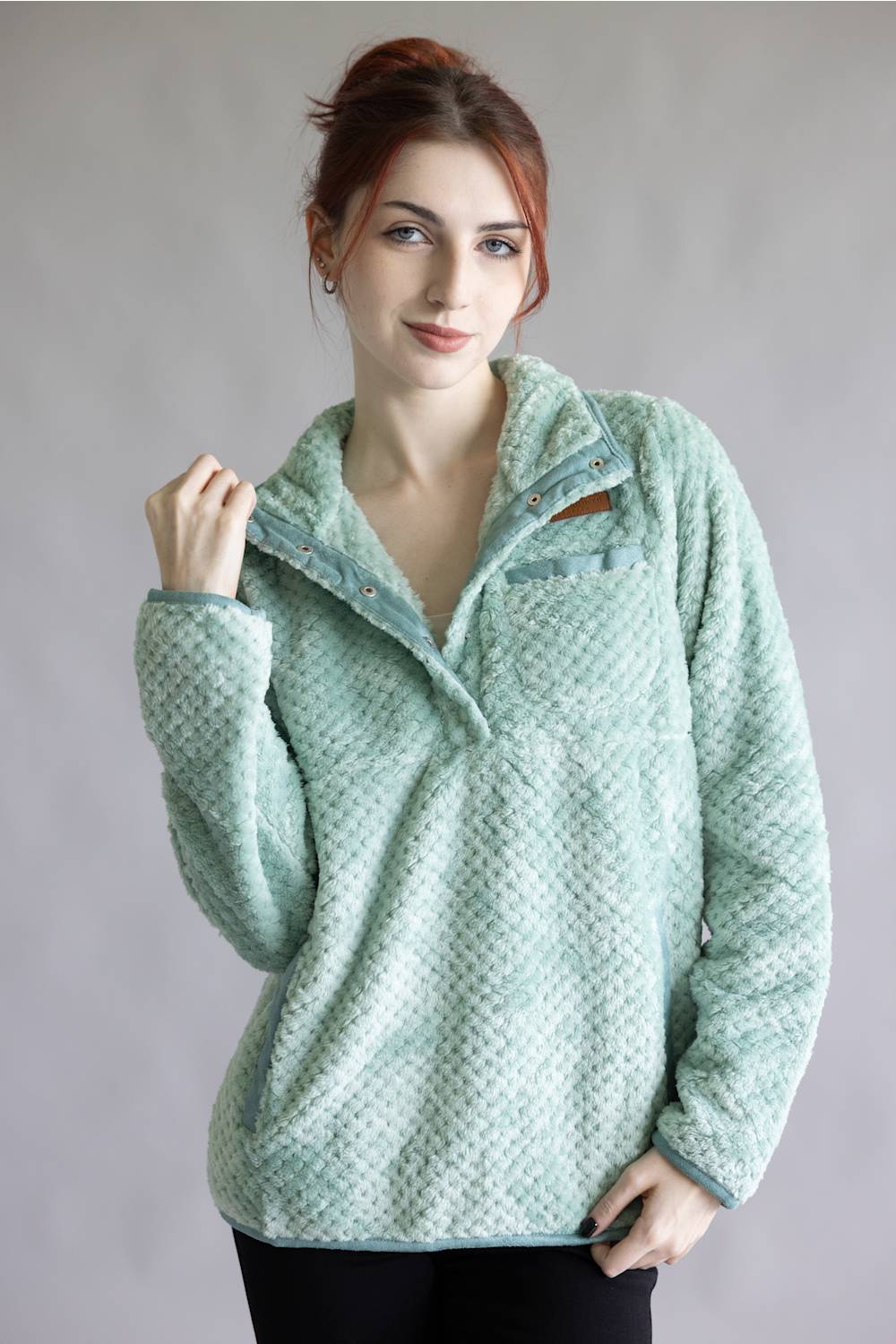 A woman wearing a light mint green textured fleece pullover with a half-zip collar, standing against a neutral gray studio background.