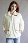 A woman with red hair wearing a cream-colored textured fleece pullover jacket with a stand-up collar, snap buttons, and a chest pocket with a brown leather accent, paired with light blue jeans, against a plain gray studio background.