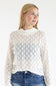 A woman wearing a white lace mock-neck long-sleeve top and blue jeans, photographed against a plain white studio background.