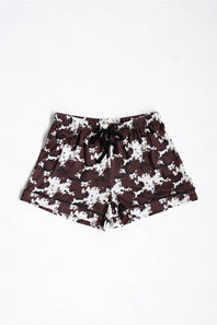 A pair of youth girls shorts featuring a dark brown and white cow pattern, with a black drawstring at the elastic waistband, laid flat against a white background.