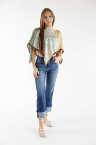 A woman modeling a lightweight poncho-style top with a multicolor abstract print in sage green, cream, and tan, paired with blue jeans and beige flat sandals, against a plain white studio background.