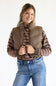 A woman wearing a brown puffer vest over a brown and red striped knit sweater, paired with blue jeans, photographed against a plain white studio background.