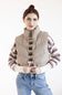 A woman wearing a beige puffer vest over a striped knit sweater and blue jeans, standing against a plain white studio background.