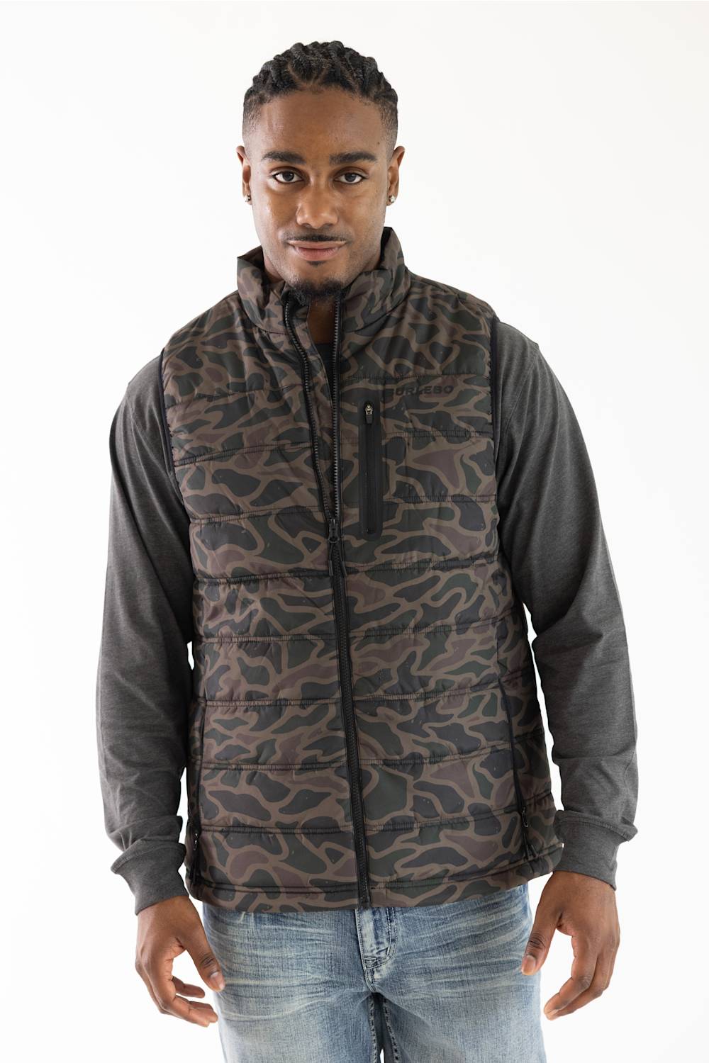 A man wearing a brown and black camouflage patterned puffer vest over a dark gray long-sleeve shirt and blue jeans, photographed against a plain white studio background.