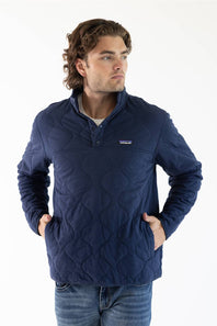 A man wearing a navy blue Patagonia quilted pullover jacket with a stand collar and zippered chest pocket, paired with blue jeans, against a plain white studio background.
