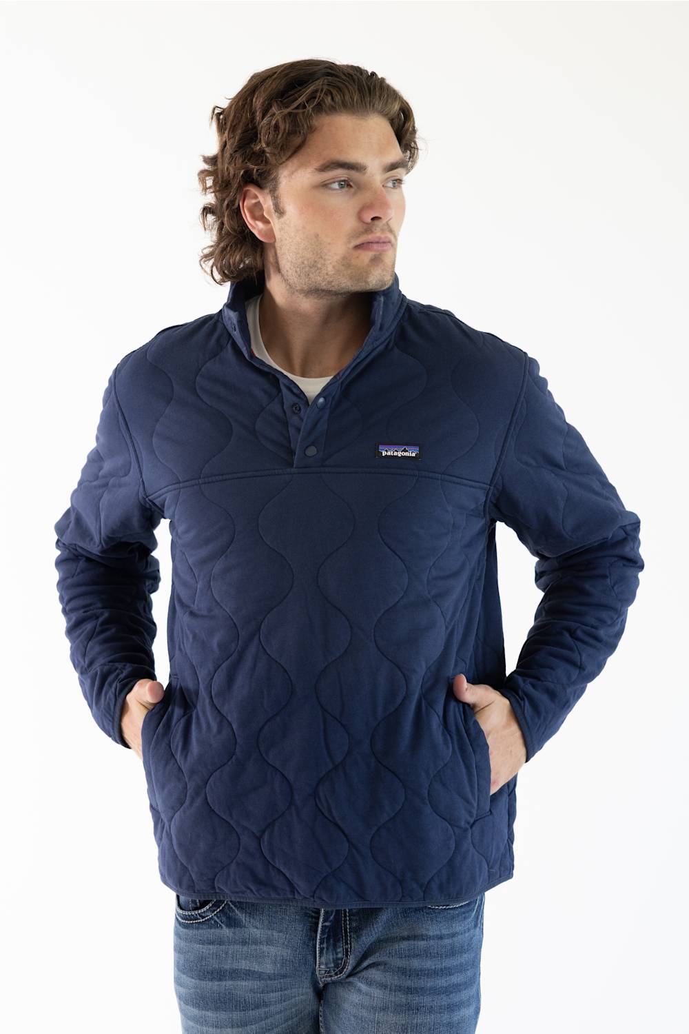 A man wearing a navy blue Patagonia quilted pullover jacket with a stand collar and zippered chest pocket, paired with blue jeans, against a plain white studio background.