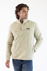 A man wearing an off white Patagonia quilted pullover jacket with a stand collar and zippered chest pocket, paired with blue jeans, against a plain white studio background.