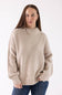 A woman modeling the Pink Rose Mock Neck Sweater in Heather Oatmeal, featuring a ribbed mock neck, drop shoulders, and long sleeves with ribbed cuffs, paired with dark-wash jeans.