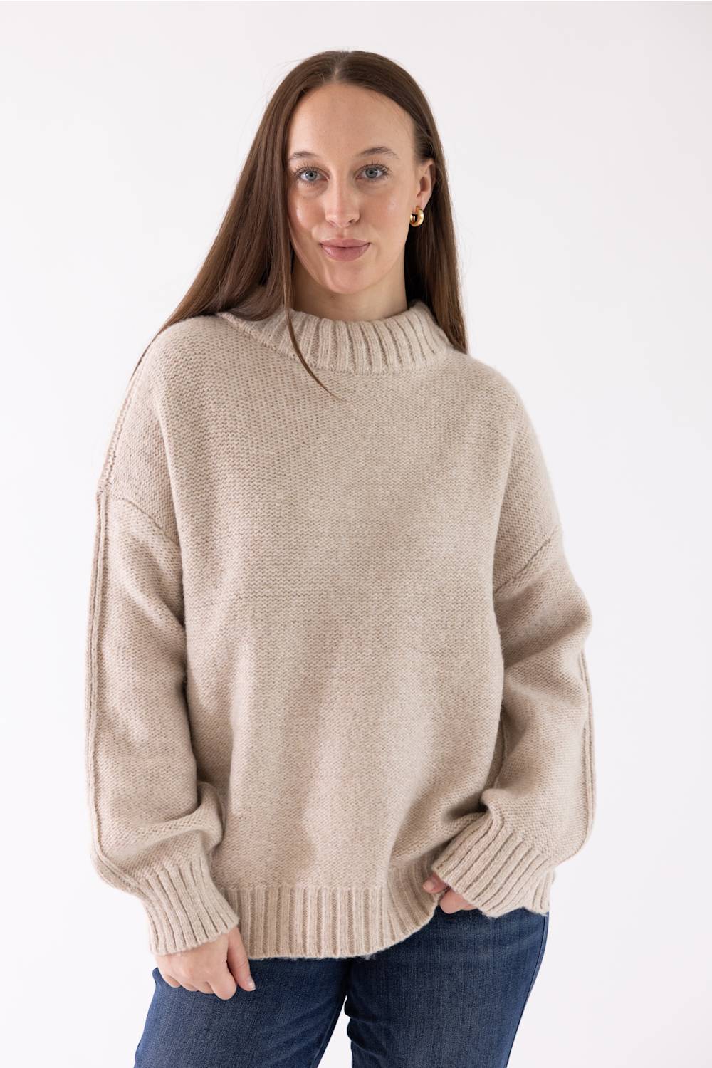A woman modeling the Pink Rose Mock Neck Sweater in Heather Oatmeal, featuring a ribbed mock neck, drop shoulders, and long sleeves with ribbed cuffs, paired with dark-wash jeans.