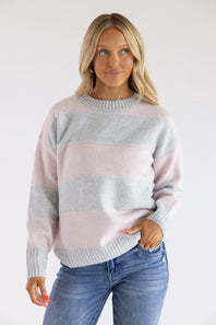 Front view of a blonde woman wearing the Pink Rose light pink and heather grey horizontal striped crew neck sweater, styled with denim jeans.