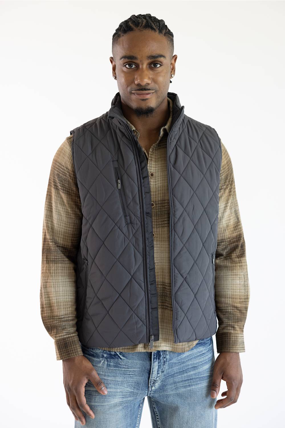 A man wearing a dark gray diamond-quilted zip-up vest over a brown and beige plaid button-up shirt, paired with blue jeans, against a plain white background.