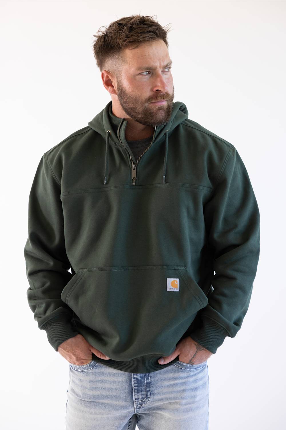Model wearing a men's dark green forestry hoodie with hands in front pockets paired with light wash denim jeans.