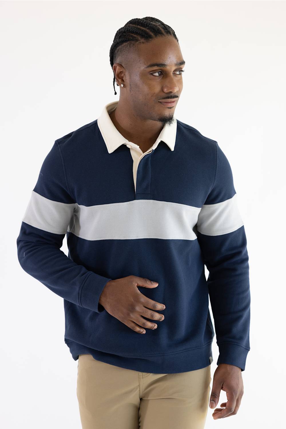 A man wearing a navy and grey color-blocked long-sleeve rugby shirt with blue jeans, standing against a plain light background.