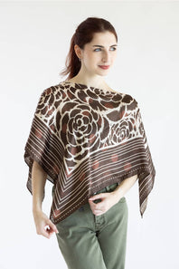 A woman modeling a brown and beige floral patterned sheer poncho top paired with olive green pants, set against a plain white studio background.