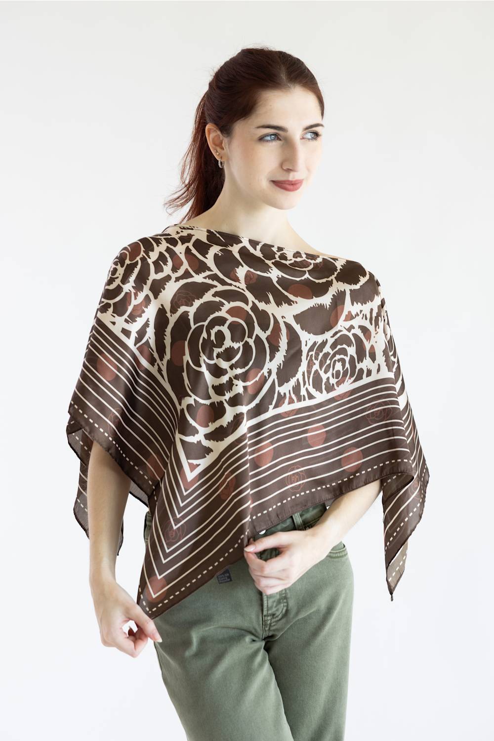 A woman modeling a brown and beige floral patterned sheer poncho top paired with olive green pants, set against a plain white studio background.