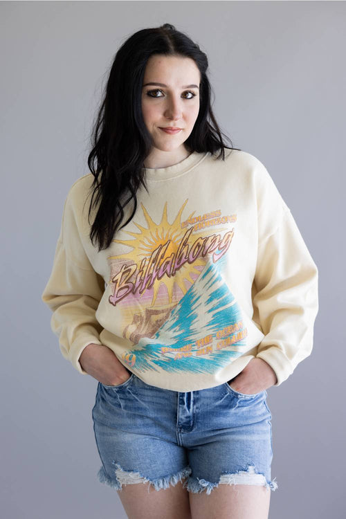 Woman wearing a beige sweatshirt with a graphic design on a plain background