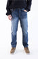 A person wearing medium-wash blue denim jeans with a dark ribbed sweater and brown shoes, standing against a plain white studio background.